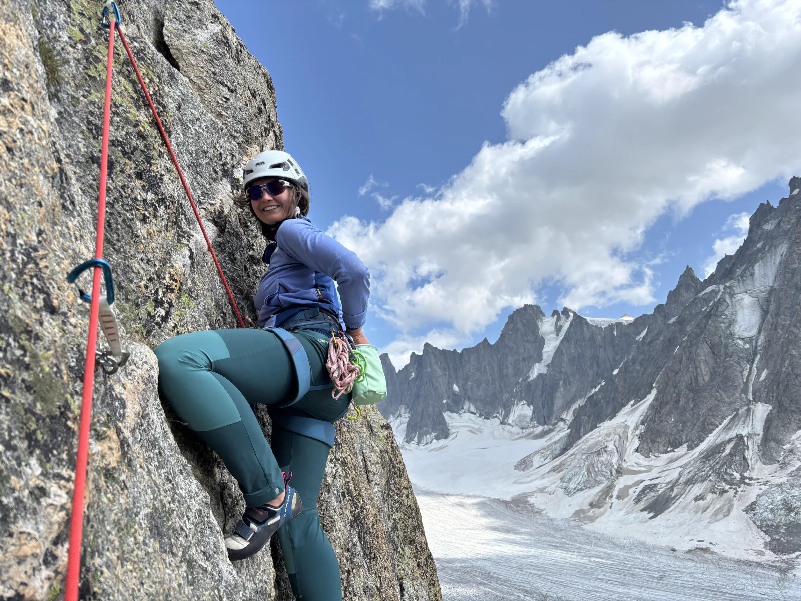 Leandra leading a pitch with high mountains in the background